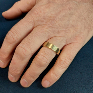 Close up shot of a mans hand wearing the wide gold wedding band with organic finish. 