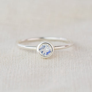 A silver ring with a clear gemstone sits on a textured cloth background