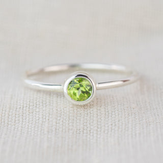 A silver ring with a green gemstone sits on a textured cloth background