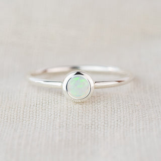 A silver ring with a whitegemstone sits on a textured cloth background
