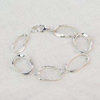 A polished silver link bracelet with irregular, organic-shaped oval links, displayed on a textured off-white linen background.