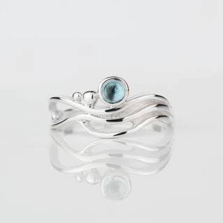 Silver ring with a blue gemstone on a light gray background