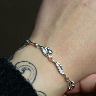 Silver bracelet on a wrist with a tattoo, against a dark background