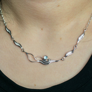 Silver necklace with a small green gemstone on a black background