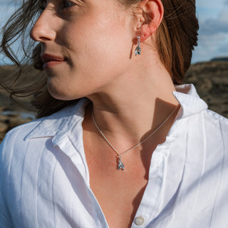 Close-up of a woman wearing silver earrings and a necklace with a scenic background