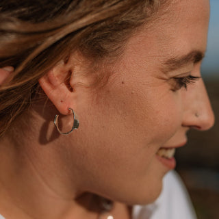 Close-up of a woman's profile with earrings and a necklace, blurred background