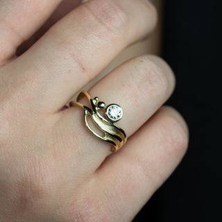 Gold ring with a diamond on a person's finger against a dark background