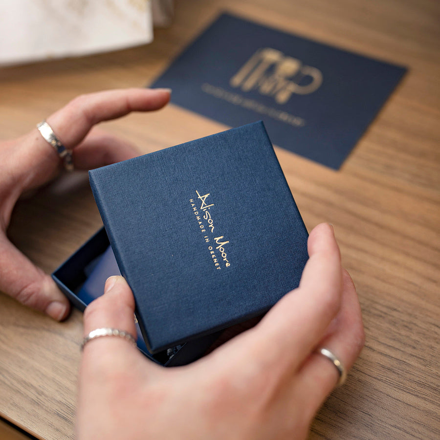 The image shows the Alison Moore Designs navy and gold branded boxes. Each order is packed with care and includes a care card and collection cards, making a great gift. 