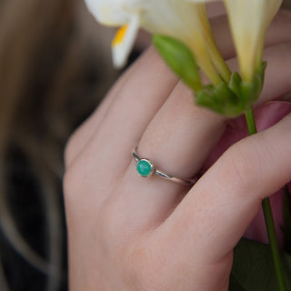 Hand wearing a silver ring with a green gemstone holding a white flower.