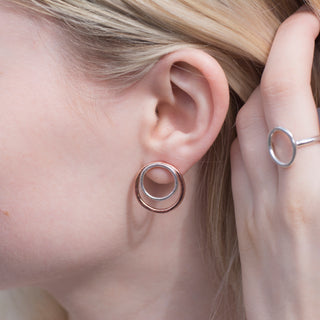 Modelled image of copper and sterling silver circle stud earrings worn on the ear alongside an Organic Circle ring, showing the contrasting metal circles and lightly hammered organic texture.