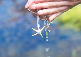 Hand holding a silver necklace with a starfish pendant against a blurred natural background