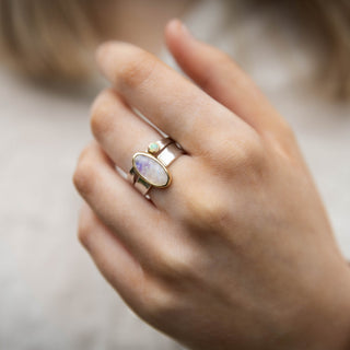 A hand wearing the Mirror Mirror Rainbow Moonstone Ring stacked with a Opal Tess ring, both in 9ct gold and sterling silver by Alison Moore Designs