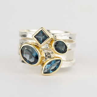 A stack of four London Blue Topaz Storybook rings in sterling silver and 9ct gold, featuring oval, diamond, round and marquise-cut gemstones, by Alison Moore Designs