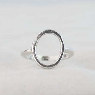 A sterling silver circle ring resting on linen. The ring has a hammered, organic texture. 

