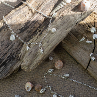 Silver chain necklace with seashell pendants on a piece of driftwood with shells on a sandy background
