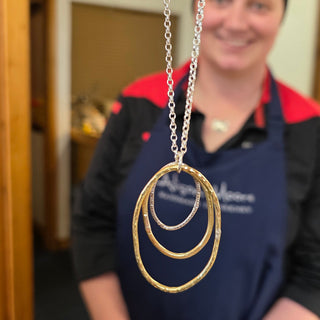 Person holding a necklace with a large circular pendant in a store setting