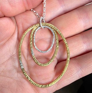 Gold and silver circular pendant necklace held in a hand.