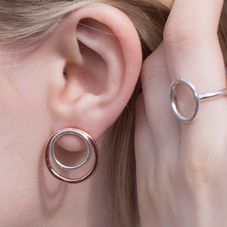 Close-up of an ear wearing a copper and silver hoop earring with a hand holding a silver ring.